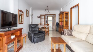 A living room with a television, leather chair, sofa, wooden coffee table, and a dining area with chairs and a table.