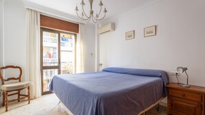 A bedroom with a bed, a wooden nightstand, a chair, a chandelier, and a balcony view.