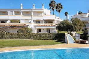 A poolside view of a hotel with a clear blue pool, white buildings with balconies, and a well-maintained lawn. - Holiday Home "Primavera" with Sea View, Pool, Wi-Fi, A/C, Terraces & Garden (Carvoeiro)