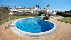 A swimming pool with a metal ladder, surrounded by a paved deck, and a large building with multiple balconies in the background. - Holiday Home "Primavera" with Sea View, Pool, Wi-Fi, A/C, Terraces & Garden (Carvoeiro)