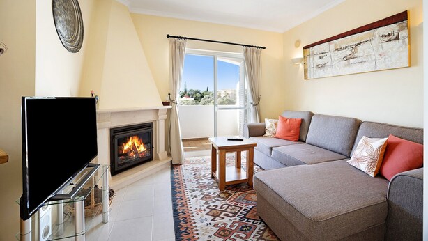 A living room with a fireplace, sofa, television, and a view of the outdoors. - Holiday Home "Primavera" with Sea View, Pool, Wi-Fi, A/C, Terraces & Garden (Carvoeiro)
