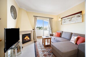 A living room with a fireplace, sofa, television, and a view of the outdoors. - Holiday Home "Primavera" with Sea View, Pool, Wi-Fi, A/C, Terraces & Garden (Carvoeiro)