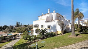 A white villa with a tiled roof, a paved driveway, and a well-maintained lawn with palm trees. - Holiday Home "Primavera" with Sea View, Pool, Wi-Fi, A/C, Terraces & Garden (Carvoeiro)