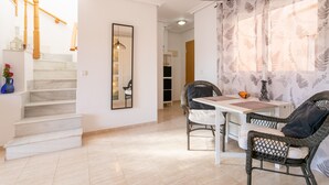 A staircase leading to a second floor, a dining area with wicker chairs and a table, and a large mirror on the wall. - Holiday Apartment with Sea View, Shared Pool & Jacuzzi, Terraces, Garden & Wi-Fi (Gran Alacant)