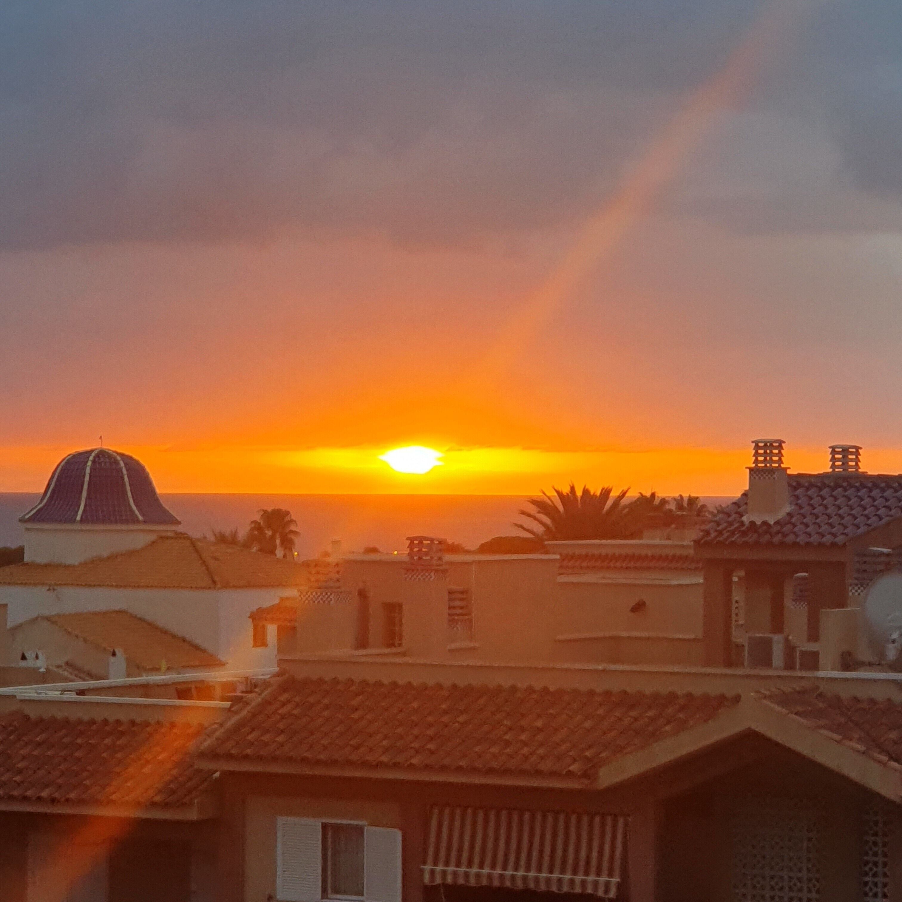 Un coucher de soleil sur une zone résidentielle, avec des bâtiments dotés de toits en tuiles et d’une structure en forme de dôme.