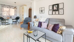 A modern living room with a grey sofa, a coffee table, and a dining area with chairs and a table. - Holiday Apartment with Sea View, Shared Pool & Jacuzzi, Terraces, Garden & Wi-Fi (Gran Alacant)
