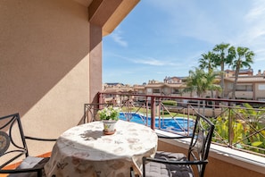 Un balcon avec une table, des chaises et une vue sur une piscine et des immeubles.