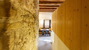 Un pasillo estrecho con paredes de piedra y vigas de madera, que conduce a un comedor con una mesa y sillas.