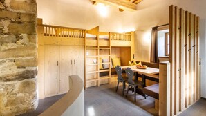 Una habitación rústica con pared de piedra, literas de madera, una mesa de comedor con sillas y un separador de madera.