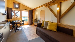 Une pièce chaleureuse avec un plafond en bois, un canapé avec des coussins, une table à manger avec des chaises et un coin cuisine.