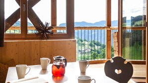 Un intérieur en bois, avec une table dressée pour le thé, et une vue sur un paysage verdoyant par de grandes fenêtres.