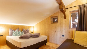 Une pièce avec un lit, un canapé, des murs en bois, une fenêtre avec des rideaux et un tableau encadré au mur.