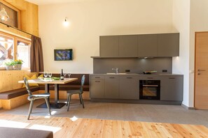 Moderni keittiö, jossa on ruokailutila, puulattia ja seinälle asennettu televisio.