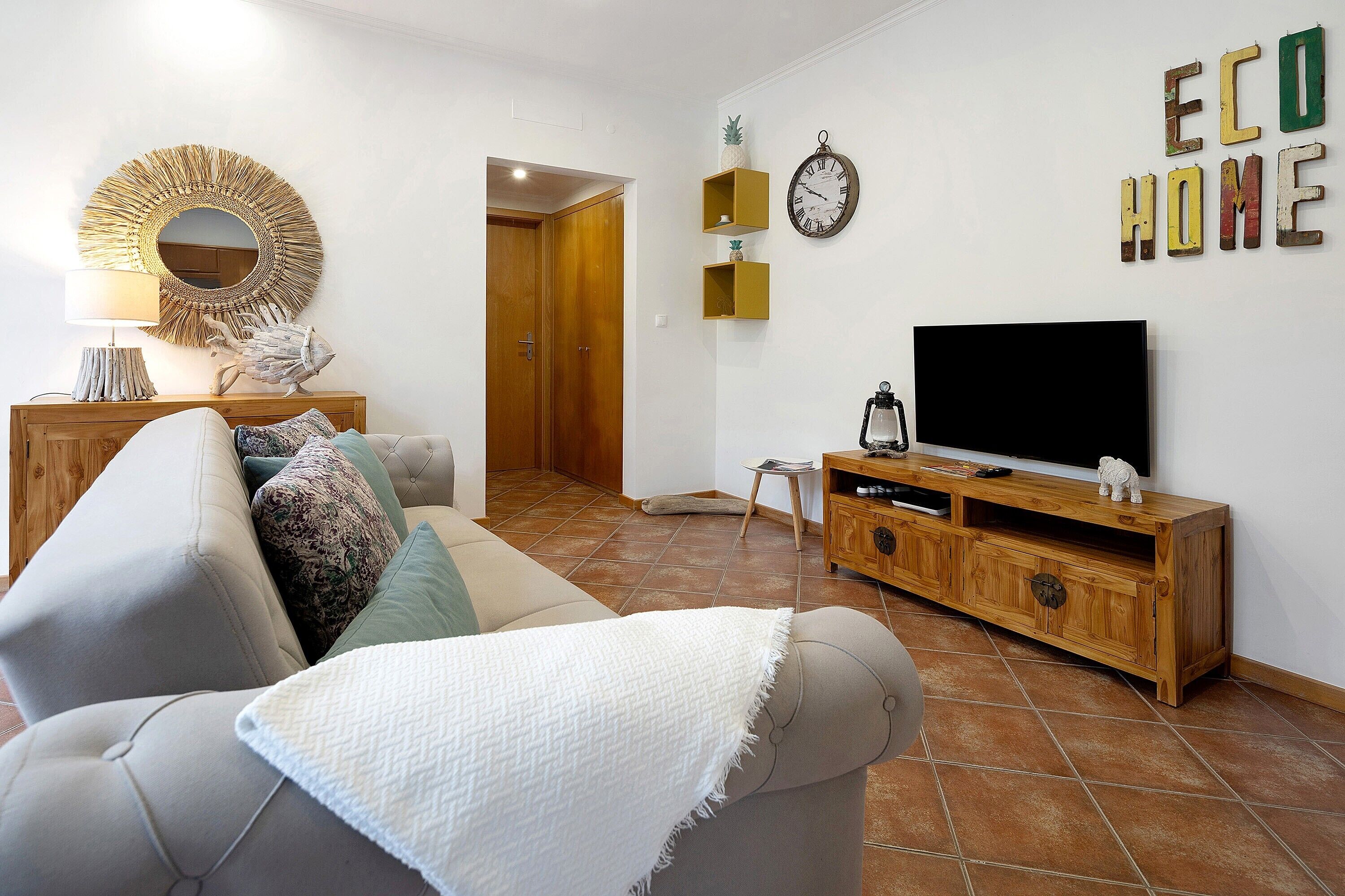 Ein Wohnzimmer mit Sofa, Fernseher, Holzschrank, Wanddekoration und einer Tür zu einem anderen Raum.