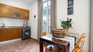 Una cocina con armarios de madera, lavadora, una mesa de comedor con sillas y una ventana con cortinas.