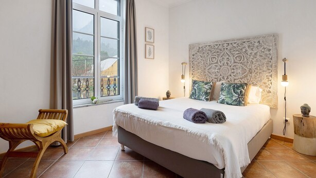 Un dormitorio con cama, una silla, un ventanal y un cabecero decorativo.