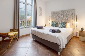A bedroom with a bed, a chair, a window, and a decorative wall headboard.