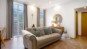 Sala de estar con un sofá, una lámpara, un espejo y vistas amplias a través de grandes ventanales.