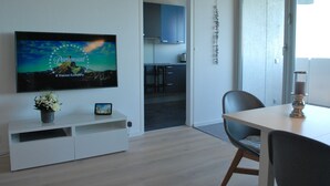 A modern living room with a flat-screen TV mounted on the wall, a small table with a candle, and a dining area with a chair. - Skyline apartment with pool 2-6 guests with Netflix (Kronberg im Taunus)