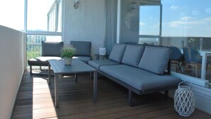 A balcony with a grey sofa, a small table, and a chair. - Skyline apartment with pool 2-6 guests with Netflix (Kronberg im Taunus)