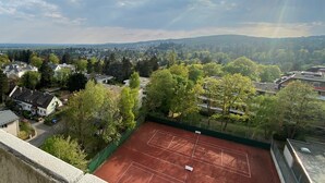 A tennis court surrounded by trees and houses, with a view of a town and hills in the distance. - Skyline apartment with pool 2-6 guests with Netflix (Kronberg im Taunus)