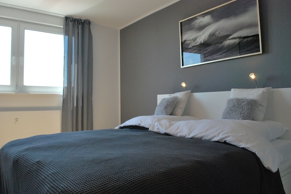 A bedroom with a large bed, a window with curtains, and a painting on the wall.