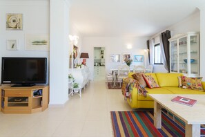 Un salon comprenant un téléviseur, un canapé jaune, une table à manger, des chaises et un meuble.