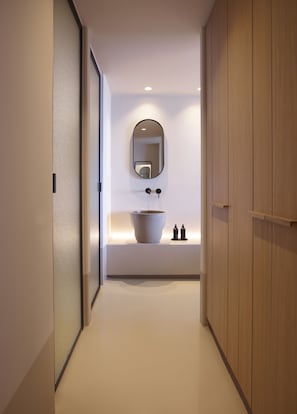 A modern bathroom with a large oval mirror, a vessel sink, and a small shelf with toiletries. - Collini Hotel Mykonos (Mykonos)