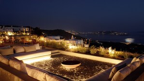 A rooftop terrace with outdoor seating, a fire pit, and a view of the coastline at night. - Collini Hotel Mykonos, WorldHotels Elite (Mykonos)