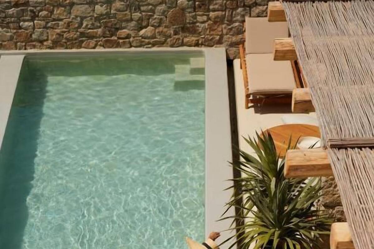 A poolside area with a clear pool, lounge chairs, and a potted plant.
