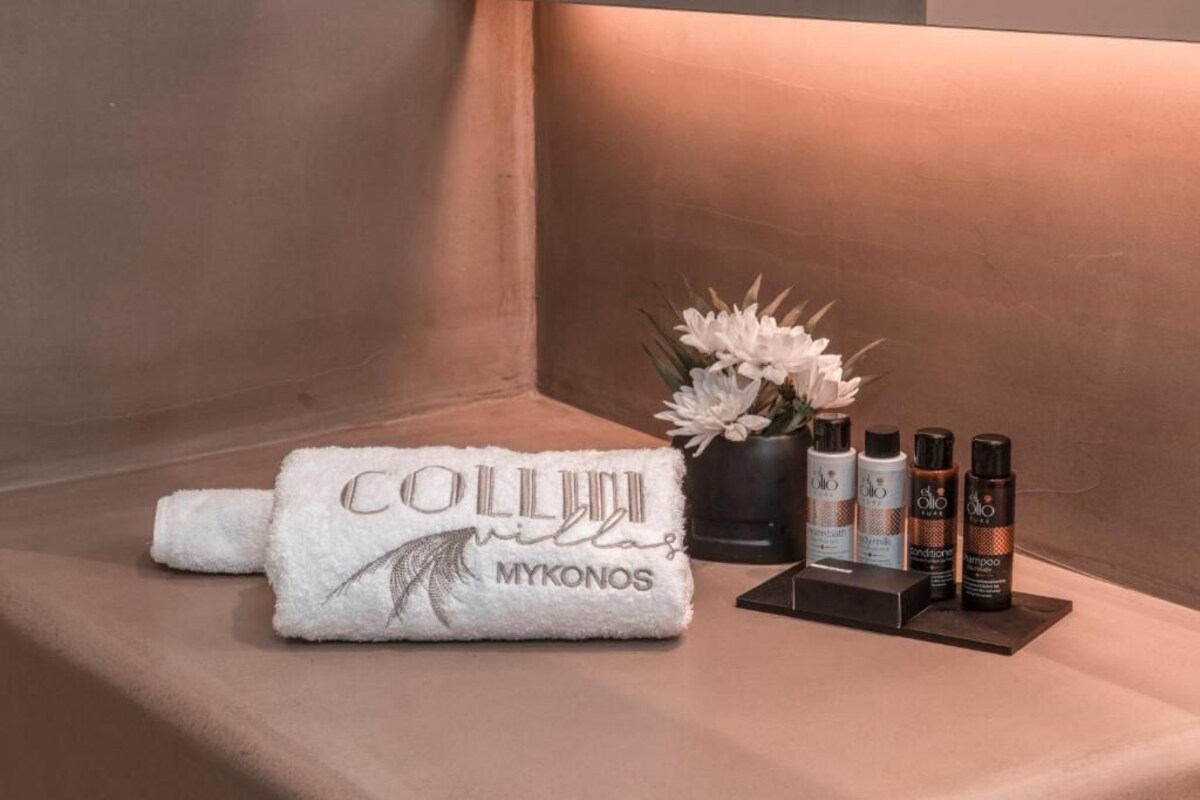 A towel with "COLLIUM MYKONOS" text, a potted plant, and three bottles of hair care products on a beige surface.