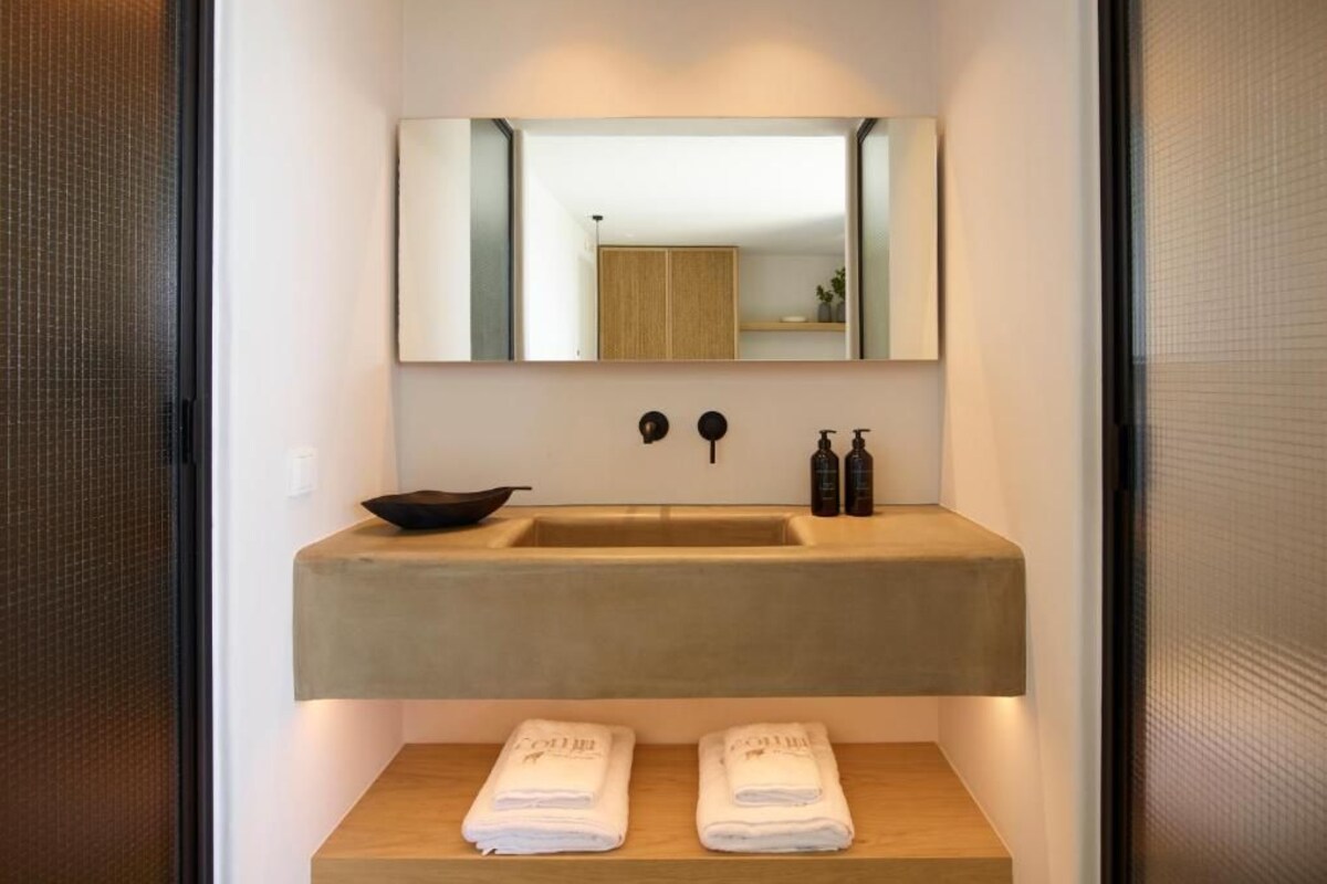 A modern bathroom with a large mirror, a beige sink, two towel racks, and two bottles of soap.