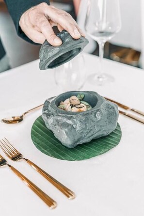 A person holding a stone bowl over a table with a green leaf underneath.