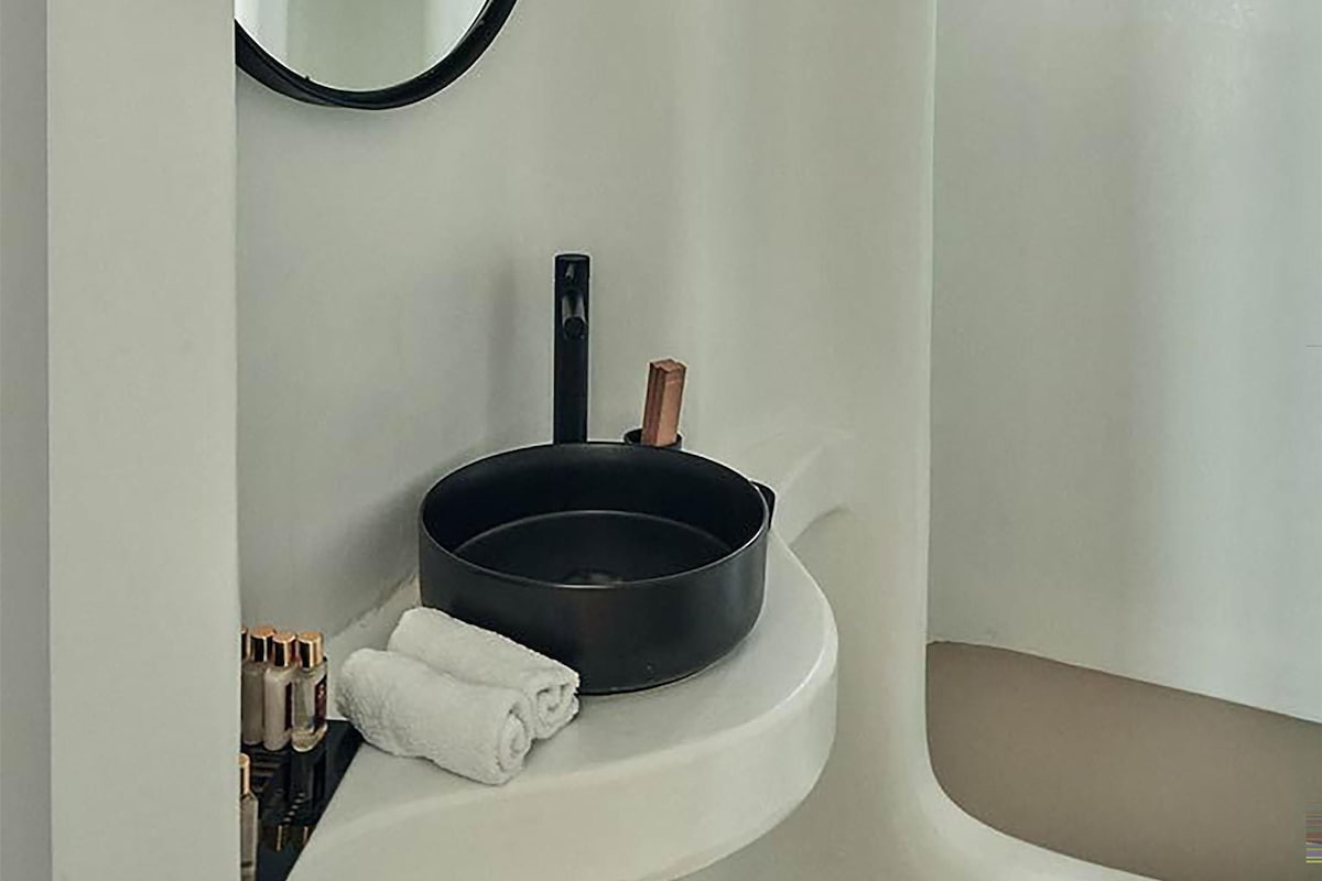 A bathroom with a round mirror, a black sink, and a window.