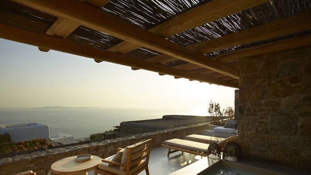 A poolside area with lounge chairs, a table, and a view of the sea. - Collini Hotel Mykonos, WorldHotels Elite (Mykonos)