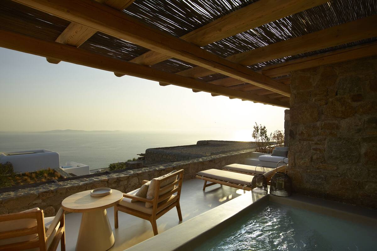 A poolside area with lounge chairs, a table, and a view of the sea.