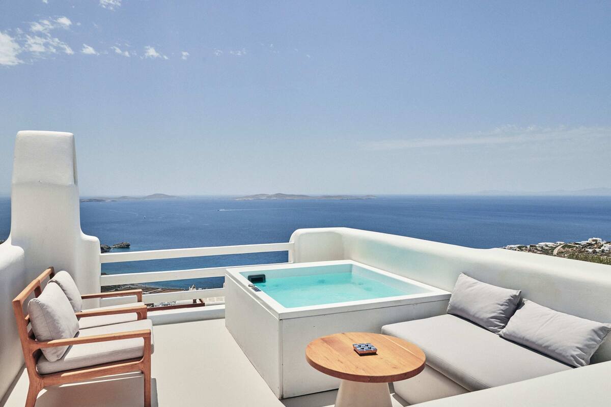A balcony with a hot tub, seating area, and a view of the sea.