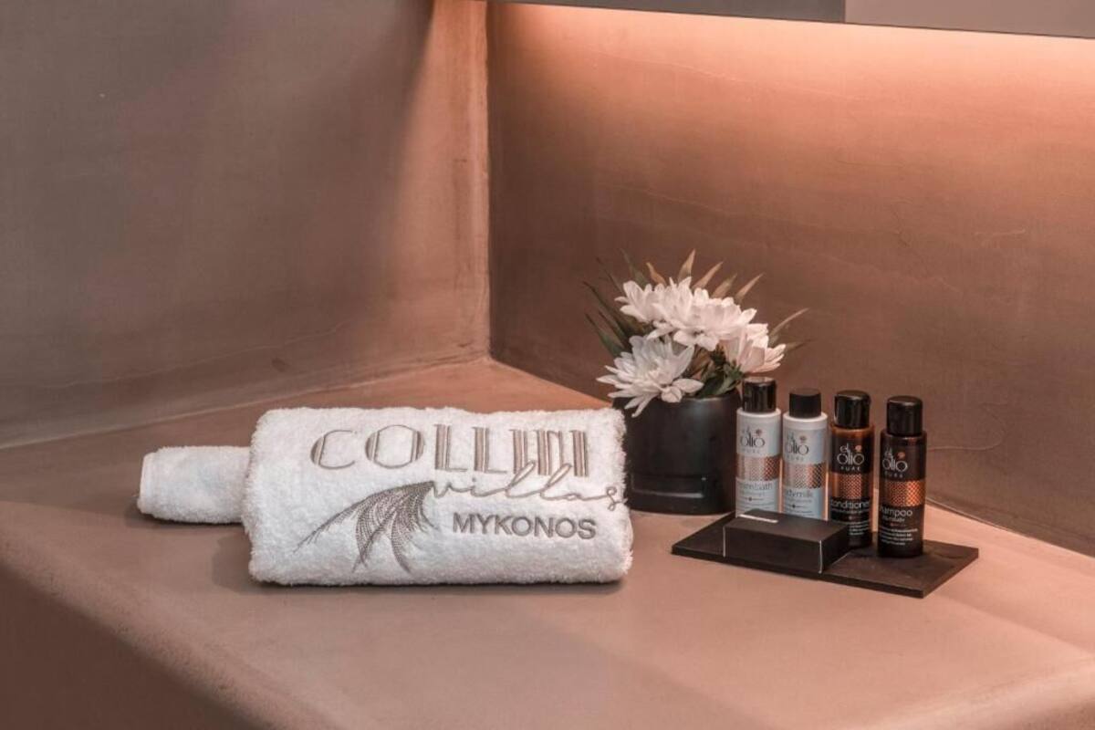 A towel with "COLLIUM MYKONOS" text, a potted plant, and three bottles of hair care products on a beige surface.