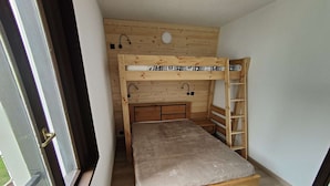Ein kleiner, kompakter Raum mit einem Etagenbett, einer Holzleiter und einem Fenster.