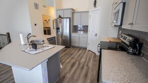 A modern kitchen with white cabinets, stainless steel appliances, and a wooden floor.