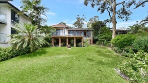 A two-story house with a balcony, surrounded by a well-maintained lawn and various trees. - Wangi Waterfront Hideaway (Wangi Wangi)