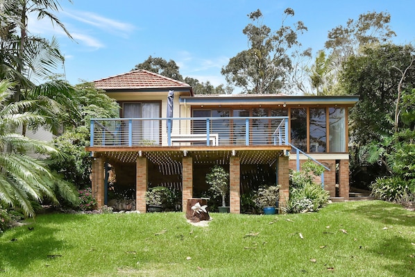 A two-story house with a balcony, surrounded by lush greenery.