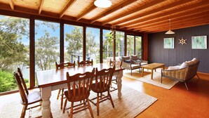 A spacious room with a large wooden dining table surrounded by chairs, a sofa, and a small table with cushions. - Wangi Waterfront Hideaway (Wangi Wangi)