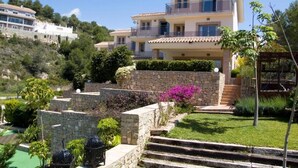 A multi-story building with a stone facade, a balcony, and a well-maintained garden with various plants and a small fountain. - Beautiful townhouse with garden, communal pool in Calpe, 4 km from the beach. (CALPE)
