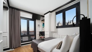 A modern hotel room with a large bed, a view of the city, and a window with curtains. - The Trinity Hotel Taksim - Special Class (Istanbul)