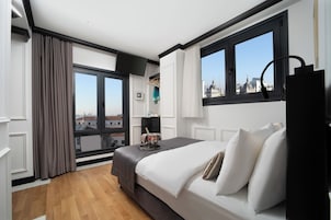 A modern hotel room with a large bed, a view of the city, and a window with curtains.