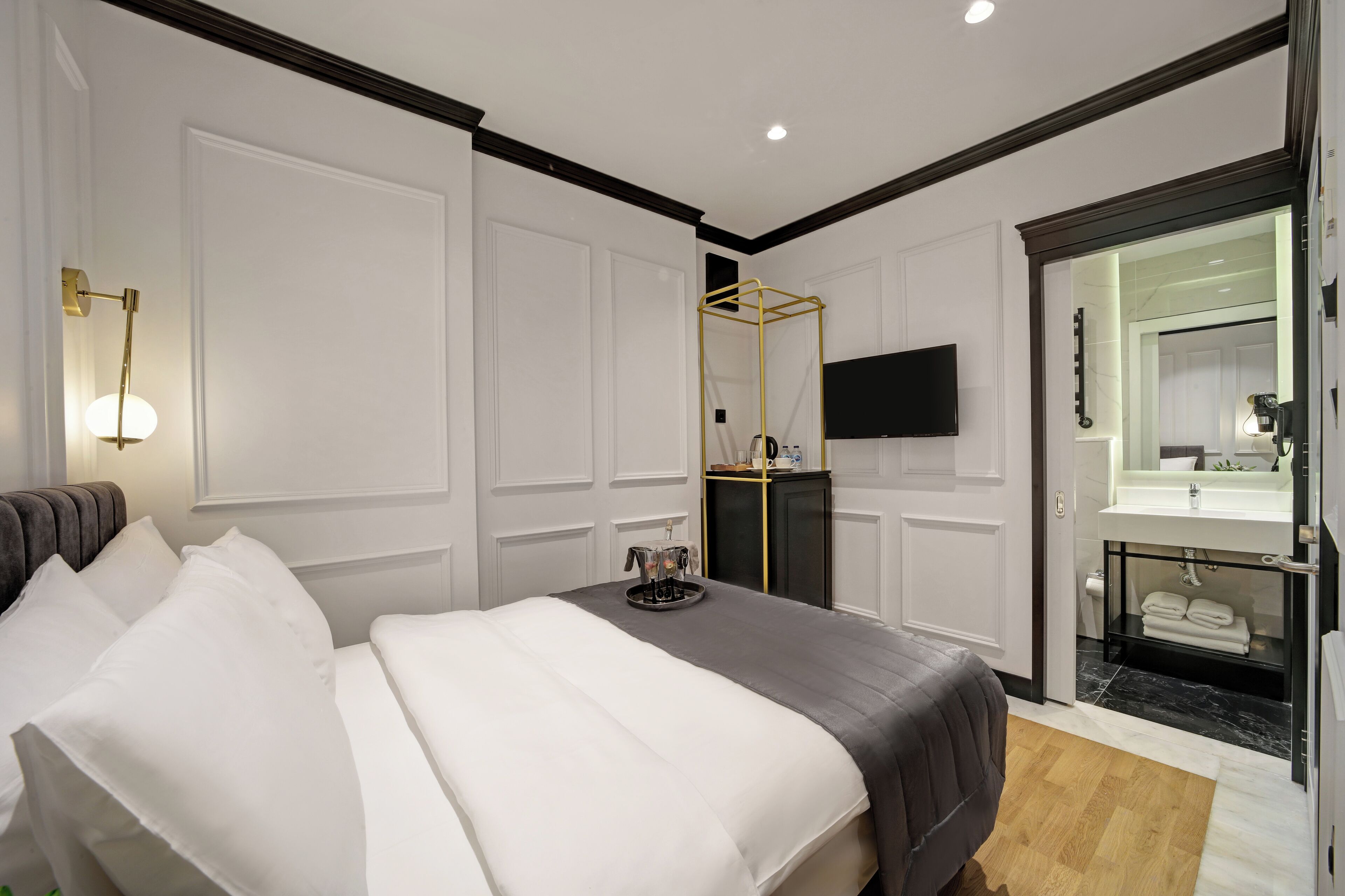 Habitación de hotel con una cama grande, una mesita de noche con bandeja, una televisión y un baño con espejo y lavamanos.