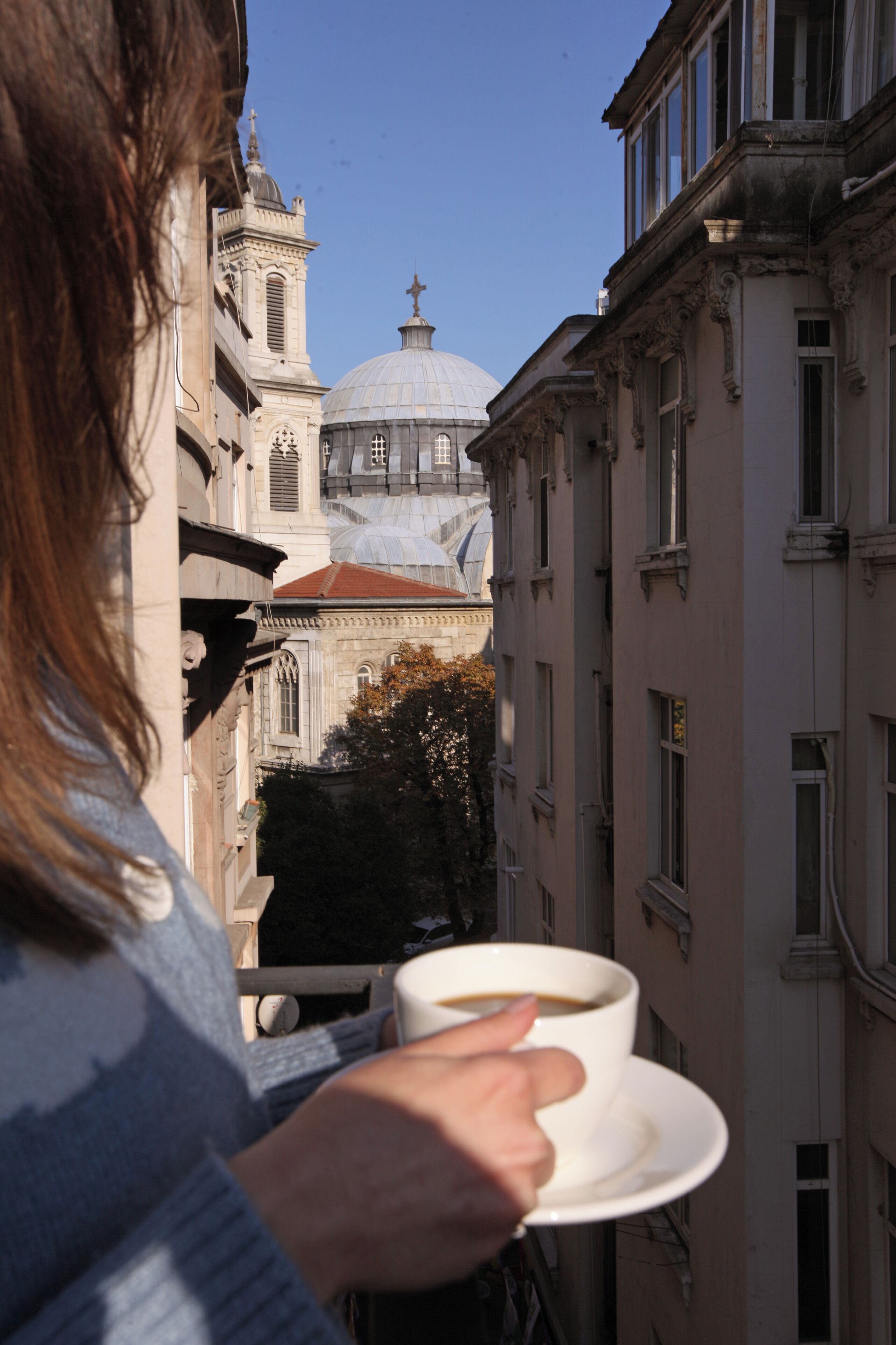 A person holding a cup of coffee, overlooking a building with a dome and bell tower.