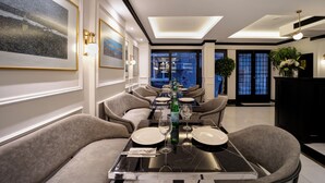 A dining area with a long table set for four, surrounded by upholstered chairs. There are framed artworks on the walls, a potted plant, and a black console table with a vase of flowers. - The Trinity Hotel Taksim - Special Class (Istanbul)