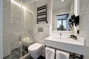 A modern bathroom with a glass-enclosed shower, a white toilet, a vanity with a mirror, and a towel rack. - The Trinity Hotel Taksim - Special Class (Istanbul)